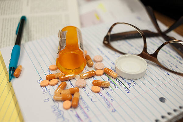 Spilled Adderall pills from prescription bottle next to glasses and notepad, illustrating addiction and treatment|Blue ADHD medication pills arranged to spell out "ADHD" on a light surface, with prescription bottle visible, highlighting the issue of prescription stimulant abuse|Close-up of a hand holding a single orange and white capsule, likely a prescription stimulant such as Adderall, against a neutral background|Young woman in pink sweater covering her face with her hand, showing signs of fatigue and distress potentially related to Adderall addiction|Close-up of two people holding hands during a therapy session, with one person wearing a blue shirt and the other a white top, symbolizing support and understanding in addiction recovery|Infographic showing 8 different Adderall pills and capsules with various colors, shapes, and markings, illustrating what Adderall looks like|Close-up of a young woman about to take an Adderall pill, illustrating the personal struggle with prescription stimulant addiction|Infographic on Adderall use and abuse, detailing its medical use for ADHD, why it's called 'the study drug', signs of addiction, and treatment options including CBT