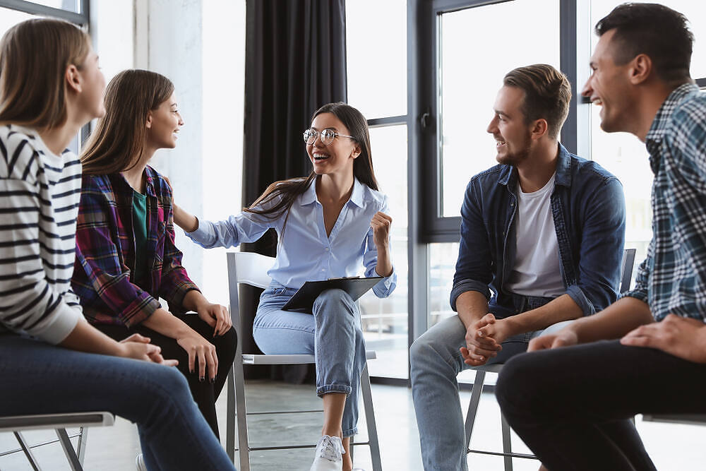 Diverse group of young adults engaged in a supportive therapy session, smiling and interacting positively|Man using tablet for video call with doctor, illustrating remote medical consultation for addiction recovery and mental health support|Family of three - mother, father, and daughter - meeting with a counselor in a comfortable home setting, illustrating family therapy for addiction recovery