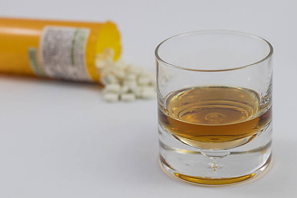 Glass of alcohol next to spilled prescription pills, illustrating risks of combining alcohol with medications|Hand holding various colorful pills with a bottle of alcohol and glass in the background, illustrating the hazardous combination of medications and alcohol|Senior male doctor in white coat holding prescription bottle, discussing medication risks with elderly female patient, emphasizing potential dangers of mixing alcohol and amoxicillin