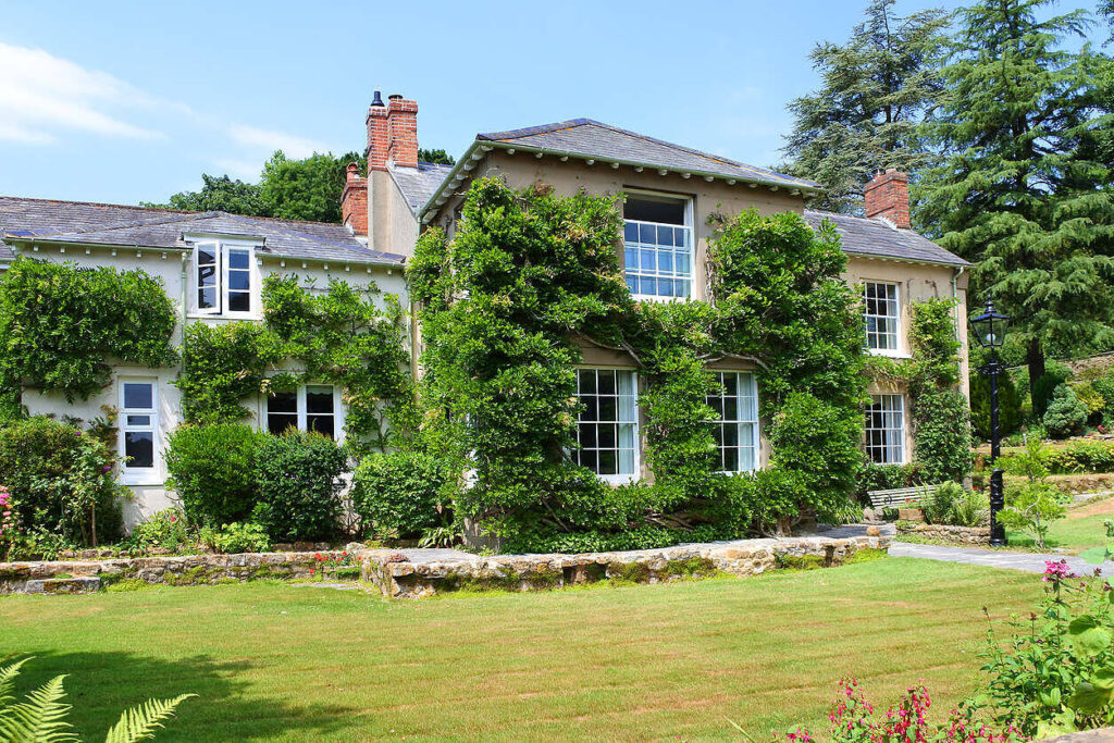 Charming English country house with ivy-covered walls, surrounded by lush gardens, ideal for alcohol rehabilitation in England|Smiling middle-aged woman with red hair in counseling session with therapist, sitting in bright room, depicting supportive environment for addiction recovery