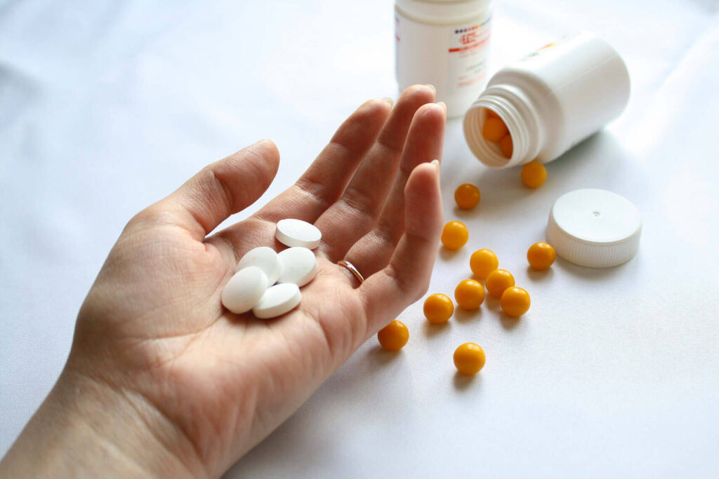 Hand holding white pills with orange pills and medication bottles in background for addiction treatment|Close-up of a metal spoon filled with dark red liquid, likely cough syrup, highlighting the potential for prescription medication abuse|Young woman with concerned expression during therapy session, sitting on couch with hand on head, facing a counselor in a bright, comfortable room|Young woman holding a bottle of red cough syrup and a dosage cup, highlighting the risks of codeine syrup misuse|Components of Lean drug mixture: bottle of codeine cough syrup, Sprite soda, candy, and a glass for mixing|Various boxes of over-the-counter pain medications including Panadeine Plus, regular Panadeine, and Nurofen Plus, highlighting potential for misuse and addiction|Young man holding a bottle of codeine cough syrup, illustrating the issue of codeine addiction among youth