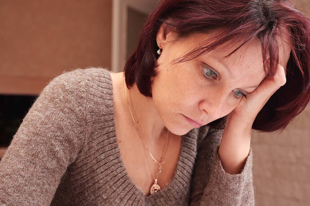 Middle-aged woman with red hair looking distressed, holding her head in her hand, depicting signs of anxiety or depression|The word 'Depression' printed on a blue background surrounded by various antidepressant pills and medication bottles|Close-up image of hands holding white pills and a glass of red wine, illustrating the dangerous combination of antidepressants and alcohol|Hand pressed against a foggy window with water droplets, symbolizing isolation, depression, and the struggle to reach out for help in addiction and mental health recovery|Wooden blocks spelling "WELLNESS" with a small plant growing between letters and smooth stones in foreground, symbolizing natural and holistic approaches to healing and recovery