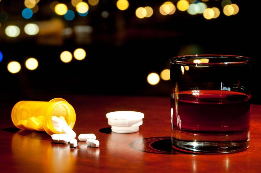 Prescription pill bottle with spilled pills next to a glass of alcohol, illustrating the dangers of combining codeine and alcohol|Close-up of a spoon filled with dark red liquid, likely codeine-based cough syrup, highlighting the risks of prescription medication abuse|Overhead view of a person holding a glass of alcohol, with a bottle and lines of white powder resembling cocaine visible on a dark surface, illustrating the dangerous combination of substances