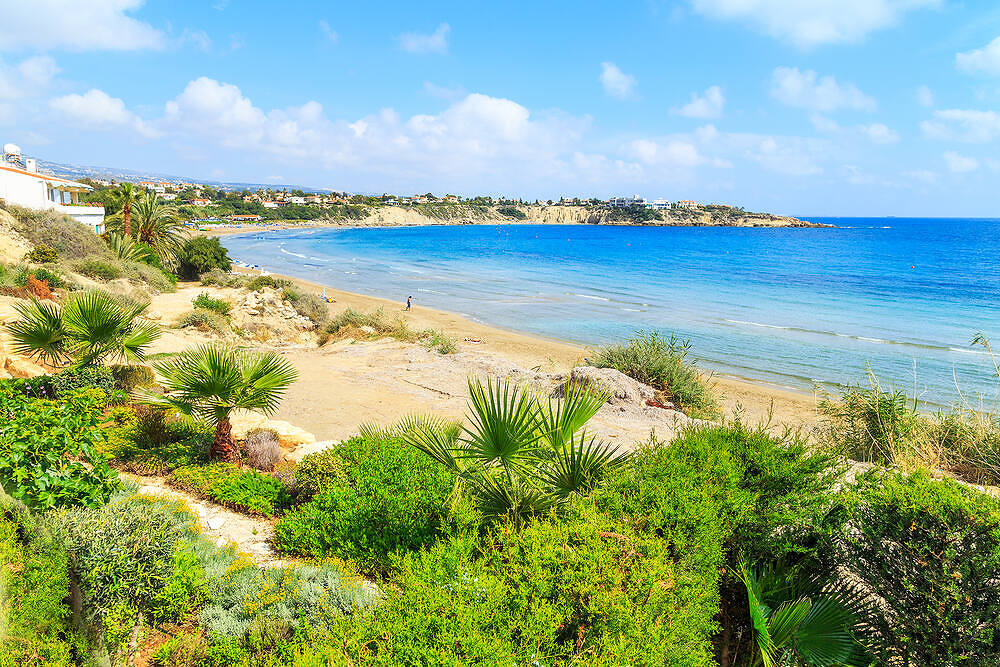 Scenic Cyprus coastline with crystal-clear blue water, sandy beach, and Mediterranean vegetation, perfect for rehabilitation|Diverse group of smiling women engaged in a supportive therapy session, illustrating the inclusive and positive environment of rehab programs in Cyprus