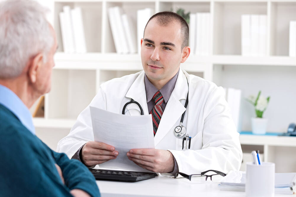Young male doctor in white coat reviewing medical documents with elderly male patient during consultation|Low-angle view of diverse hands joining together in a circle, symbolizing unity, support, and teamwork in addiction recovery groups|