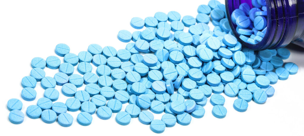 Blue Klonopin (Clonazepam) pills scattered from an open prescription bottle on a white background|Understanding Clonazepam: Chemical Structure and Addiction Treatment|Glass filled with various colorful pills and capsules, with additional pills scattered on a white surface, illustrating the issue of prescription drug abuse and polypharmacy|Young woman sitting on couch, looking sad and distressed with arms wrapped around knees, illustrating emotional struggles during addiction recovery|Person sitting on floor with prescription bottles and pills scattered in foreground, symbolizing struggle with Klonopin addiction and need for professional help|Close-up of Klonopin (clonazepam) tablets, showing the imprinted text 'CLONAZEPAM' on orange pills next to a prescription bottle|Infographic showing Klonopin's effects on the brain, prescribed uses for seizures, panic attacks, and anxiety, and its classification as a CNS depressant
