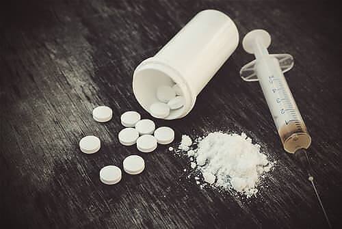Image showing prescription pills, white powder, and a syringe on a dark surface, illustrating the various forms of opioid abuse and addiction|Close-up image of various forms of opioid drugs including pills, powder, and a syringe on a dark wooden surface, illustrating the multiple routes of addiction