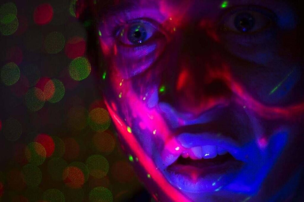 Close-up of a person's face illuminated by colorful, psychedelic lights, depicting the intense visual distortions and altered perceptions associated with PCP use|Various forms of drugs displayed including powder, pills, and syringes, illustrating the diverse nature of substance abuse and addiction challenges|Close-up of opened white pill capsules with powder spilled out on a dark surface, illustrating the misuse of prescription medications