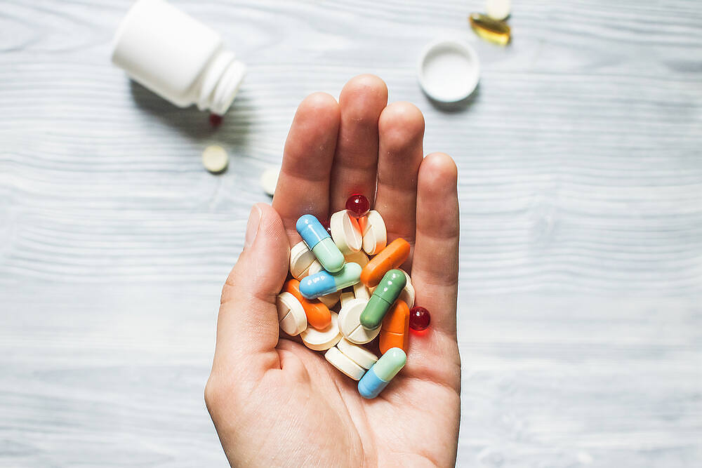 Hand holding assorted colorful prescription pills and capsules, with medication bottle in background|Close-up of individual holding a small blue pill and glass of water, about to take medication||Infographic explaining prescription opioids, their medical uses for pain management, common examples like hydrocodone and morphine, and risks including addiction and overdose|Infographic detailing codeine addiction characteristics, including its high addictiveness, effects on the body's reward system, and psychological impacts, alongside an image of a distressed woman|Shelves stocked with various prescription medications in a pharmacy, highlighting the wide availability of potentially addictive drugs|Woman in office setting experiencing back pain while working at desk, illustrating potential side effects of prescription medication use|Split image: Left shows diverse group in therapy session, right displays green-tinted hands joining in unity, representing holistic approach to addiction treatment|Pill organizer with various colorful medications, single white pill, and empty glass on blue background, illustrating prescription drug use and potential for abuse|Woman's hands holding white pills and a glass of red wine, illustrating the dangerous combination of prescription medications and alcohol||Pharmacist's hands selecting medication from pharmacy shelves, holding blister pack of blue pills, illustrating access to prescription drugs|Multiple prescription medication bottles in foreground with blurred image of distressed person holding head in background, illustrating struggle with prescription drug dependence|Infographic detailing prescription opioid uses, examples like hydrocodone and morphine, and risks including addiction and overdose, with pill icons on purple background|Infographic on prescription drug addiction showing proper use vs. addiction signs, including mood swings, overuse, and physical symptoms. Features hands pouring pills from a bottle.