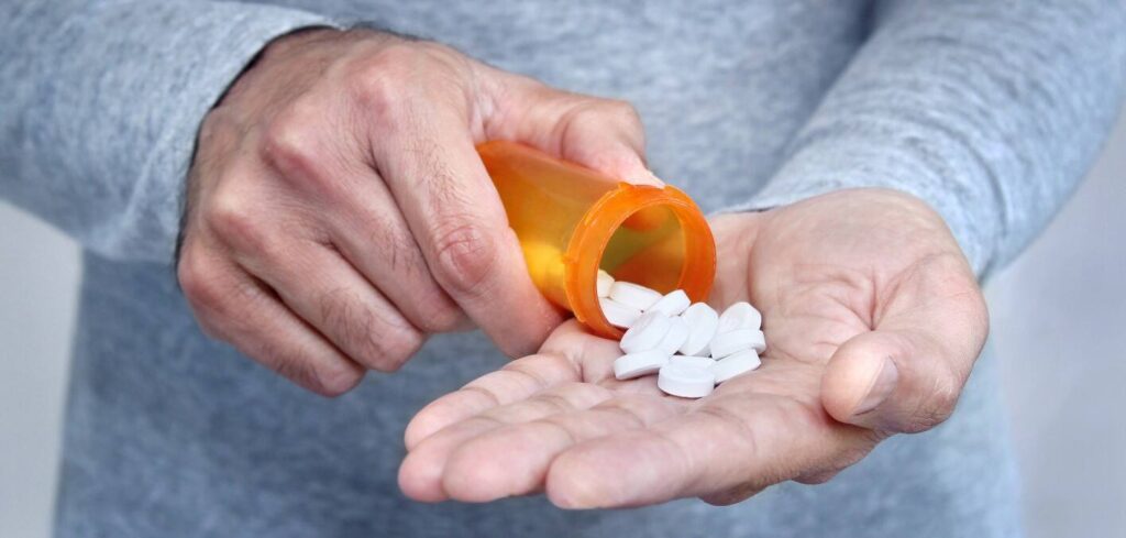 Person pouring white pills from orange prescription bottle into their palm|Graph showing increasing deaths related to pregabalin and gabapentin in England from 2007 to 2017, highlighting the dangers of prescribed drug misuse|Bar chart showing age-standardised mortality rates for drug misuse deaths across regions of England and Wales in 2018, highlighting higher rates in northern regions