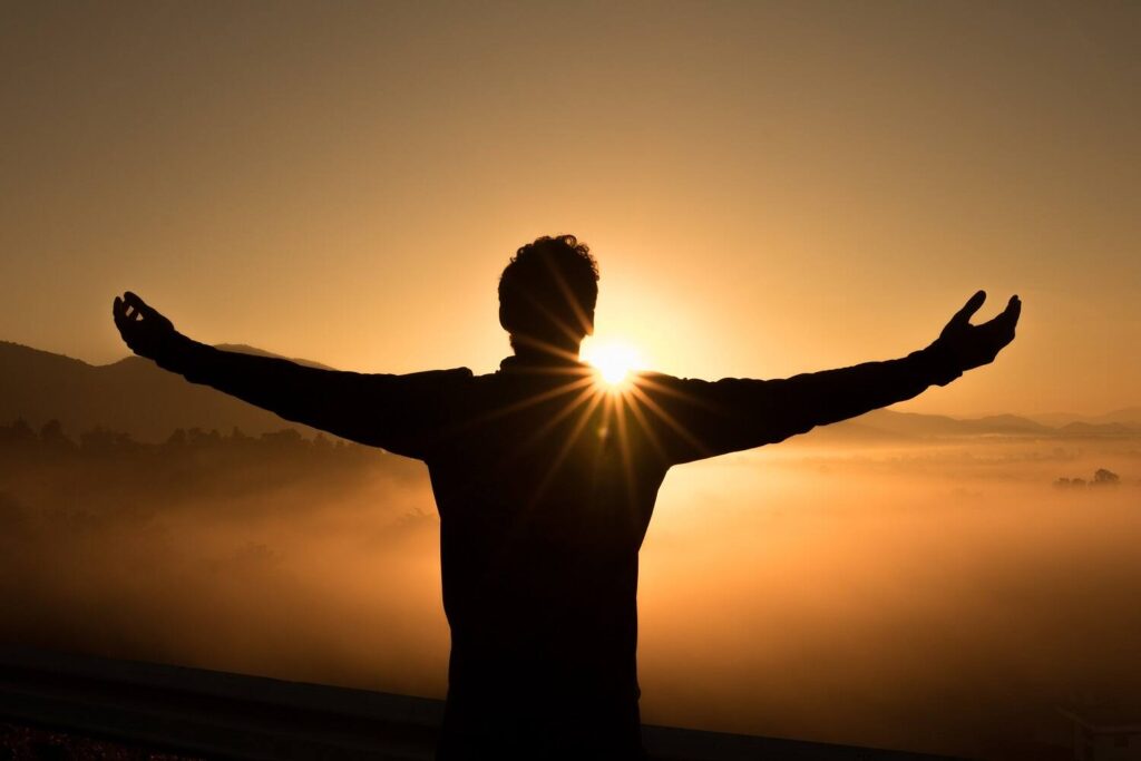 Silhouette of person with arms outstretched facing sunrise over misty landscape, symbolizing hope and new beginnings in addiction recovery|Silhouette of a woman with flowing orange scarf against sunset, symbolizing hope and freedom in addiction recovery|Woman with blonde hair sitting on a rock in a peaceful garden, reading a book, symbolizing tranquility and self-reflection in addiction recovery||