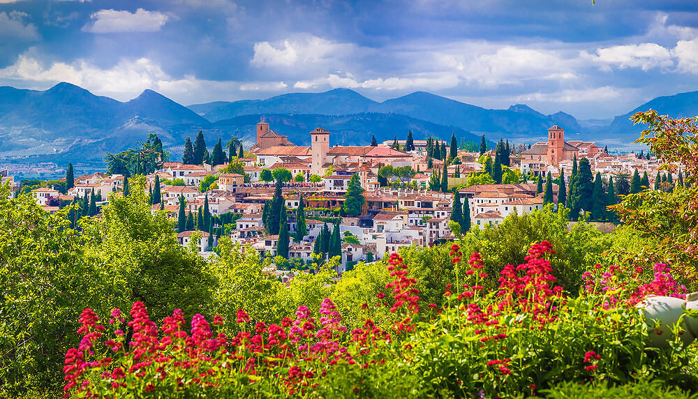 Picturesque view of a traditional Spanish village nestled in mountains, with colorful flowers in foreground, symbolizing hope and new beginnings in addiction recovery|Upscale yellow villa surrounded by lush gardens and trees, ideal for peaceful rehabilitation in Spain|Inviting pool area of a Spanish rehab center with comfortable seating, lush greenery, and a sunny yellow villa backdrop