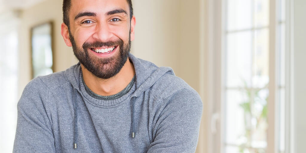 Bearded man in grey hoodie smiling confidently after drug and alcohol rehab treatment|Smiling man in glasses participating in a diverse group therapy session for drug and alcohol rehabilitation in West Sussex, with text overlay|Smiling man with glasses in a group therapy session for drug and alcohol rehabilitation in West Sussex, surrounded by diverse participants in a bright, welcoming environment|Collage showing a charming brick rehab facility exterior, group therapy room, and elegant interior hallway, representing the comprehensive alcohol rehabilitation services in West Sussex