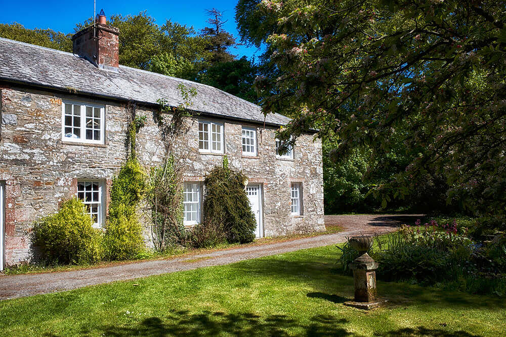 Picturesque stone cottage rehab center in rural Wales surrounded by lush greenery and trees|Diverse group of young adults sitting in a circle during a therapy session, holding coffee cups and engaging in conversation in a warm, casual rehab center setting