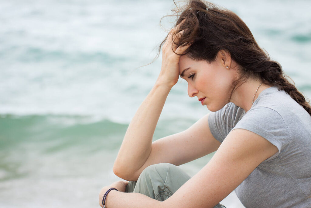 Close-up of a sad and depressed woman sitting by the beach, reflecting on her drug detox journey.||||The word 'DETOX' spelled out in cloud letters against a bright blue sky, symbolizing hope and clarity in drug recovery